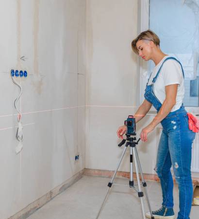 Woman makes repairs in new apartment. Builder levels walls using laser level. High quality photo